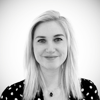 Svartvitt porträtt av leende kvinna med långt hår och prickig tröja.