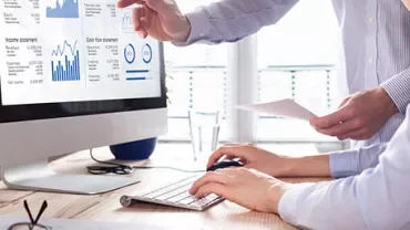 Two people analyzing financial data on a computer.