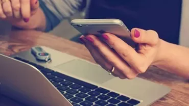 Person som håller i en smartphone över en laptop med ett USB-minne på bordet.