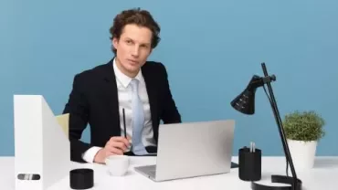 Man i kostym vid ett skrivbord med laptop och lampa