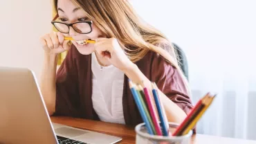 Person biting pencil while looking at laptop screen