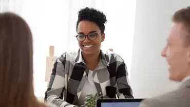 Smiling person wearing glasses at a meeting table.