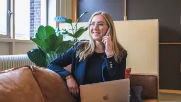 Kvinna i svart kavaj pratar i telefon med en laptop