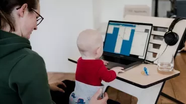 En bebis sitter i en kvinnas knä och når efter en laptop.