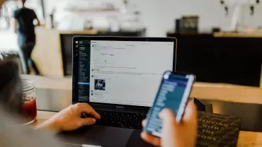 Person använder laptop och håller smartphone på ett kafé.