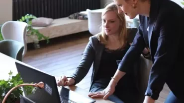 Two women collaborating at a laptop in a modern office.