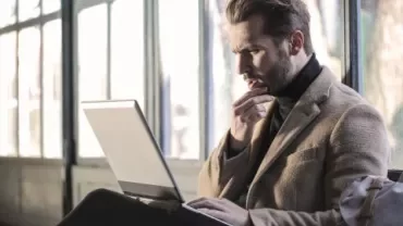 Man concentrating on a laptop in a bright room.