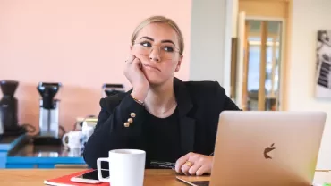 Pensive person at a desk with a laptop and coffee.