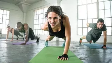 Group in a gym doing one-arm push-ups on mats.
