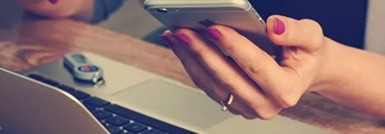 Person som håller i en smartphone över en laptop med ett USB-minne på bordet.