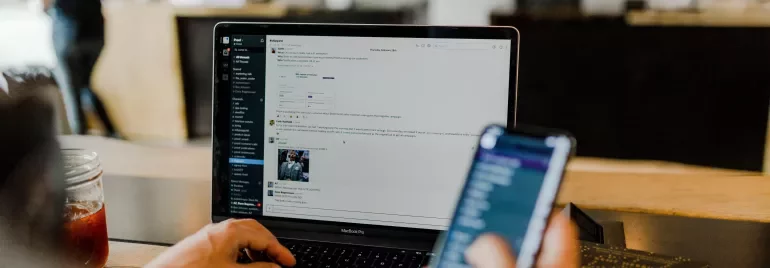 Person använder laptop och håller smartphone på ett kafé.