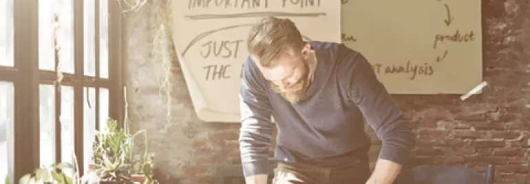 Man skriver vid ett skrivbord med växter och anteckningar på väggen.