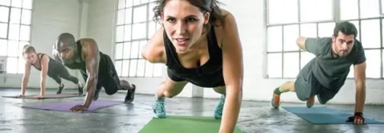 Grupp i ett gym som gör armhävningar på en arm på mattor.