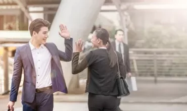 Two people in business attire high-fiving outdoors.