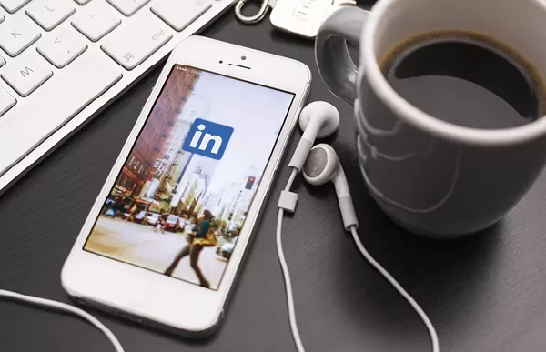 Smartphone med LinkedIn-app, hörlurar och kaffe.